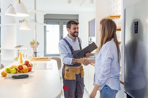 Plumber shaking hands with customer inside kitchen.