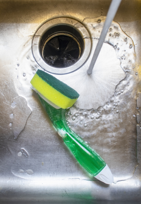 Water from tap running into stainless steel sink with pot scrubber lying in it.