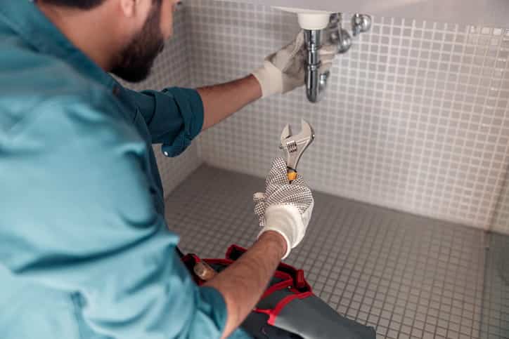 A plumber working on pipes underneath a bathroom sink.