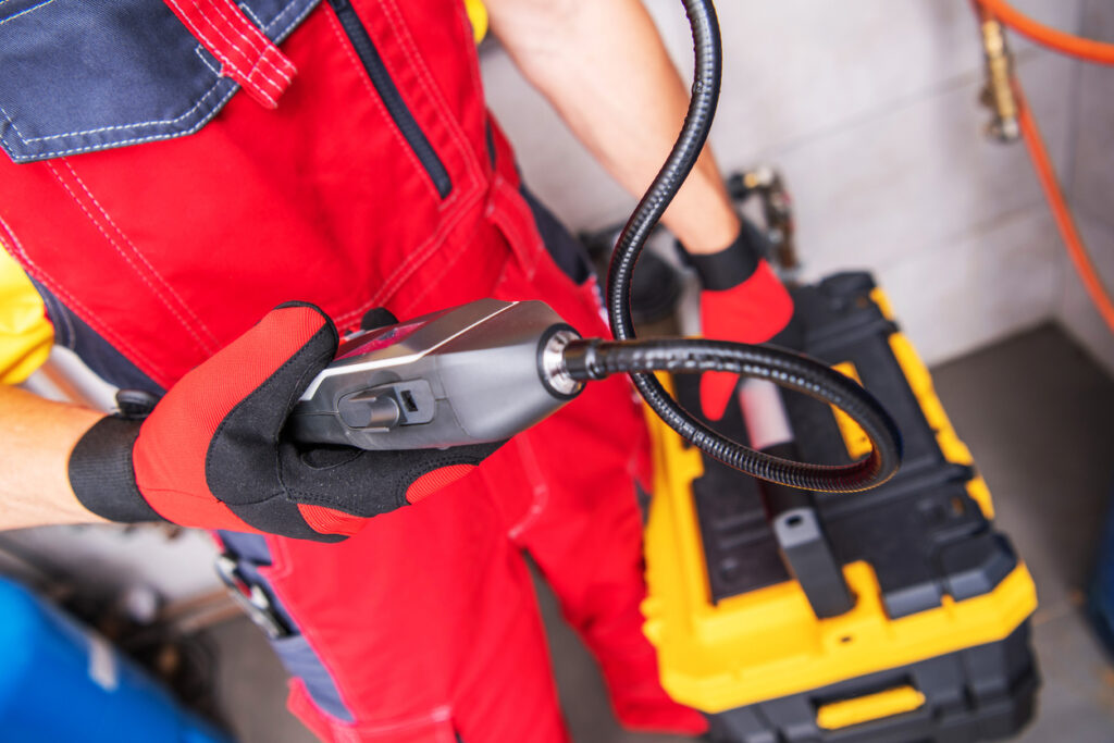 Closeup of Professional Plumber with Portable Gas Leak Detector in His Hand Checking the Efficiency of the Water Heating System in Commercial Building.