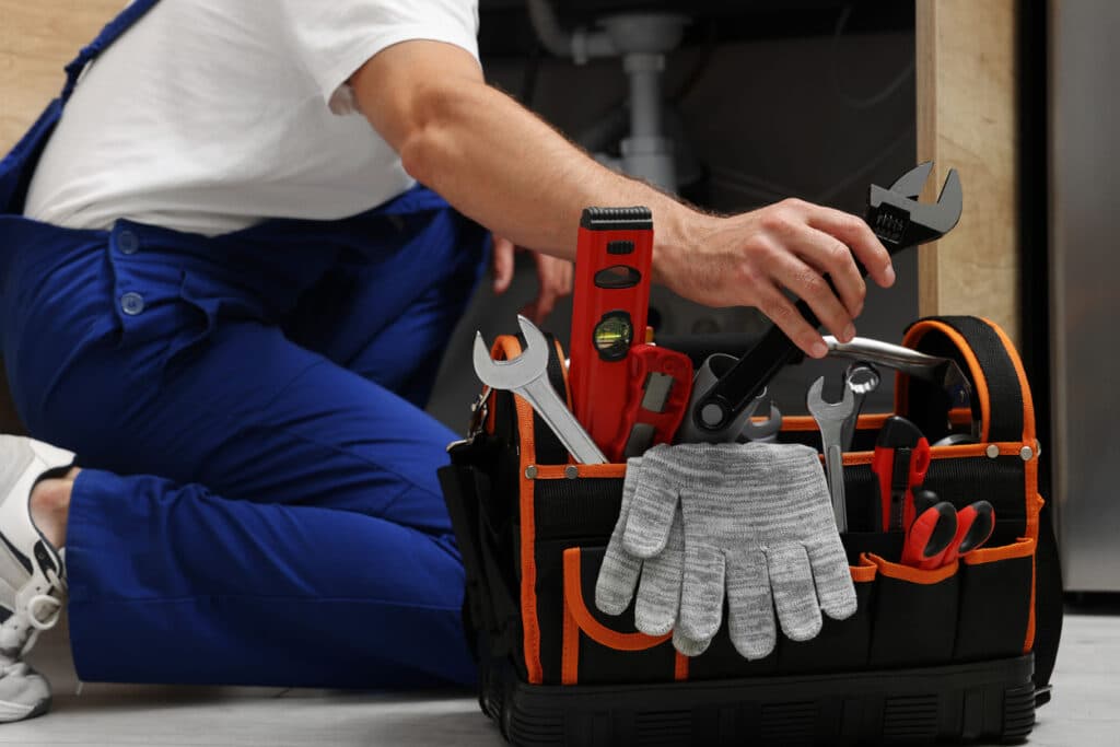 Professional plumber taking adjustable wrench from tool bag indoors